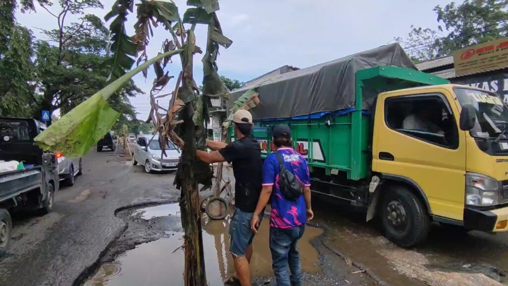 Kesal karena jalan tak kunjung diperbaiki, warga Desa Kanci, Kabupaten Cirebon, Jawa Barat, menggelar aksi protes pada Minggu pagi dengan menanam pohon pisang di lubang-lubang jalan yang rusak.